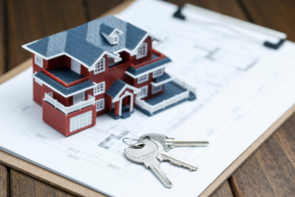 Un modèle réduit de maison sur des plans d'architecte avec des clés à côté, symbolisant la propriété immobilière et la planification de la construction.