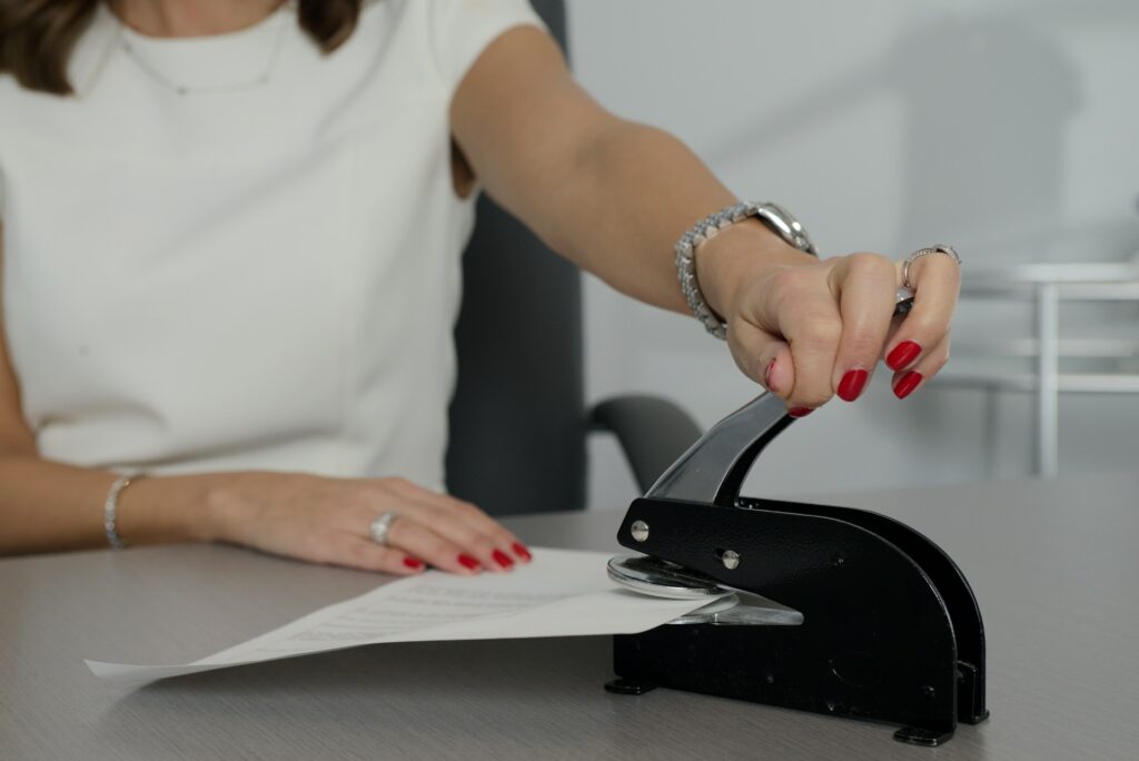 Une femme utilise une perforatrice sur un document, une action typique dans un contexte administratif ou de bureau