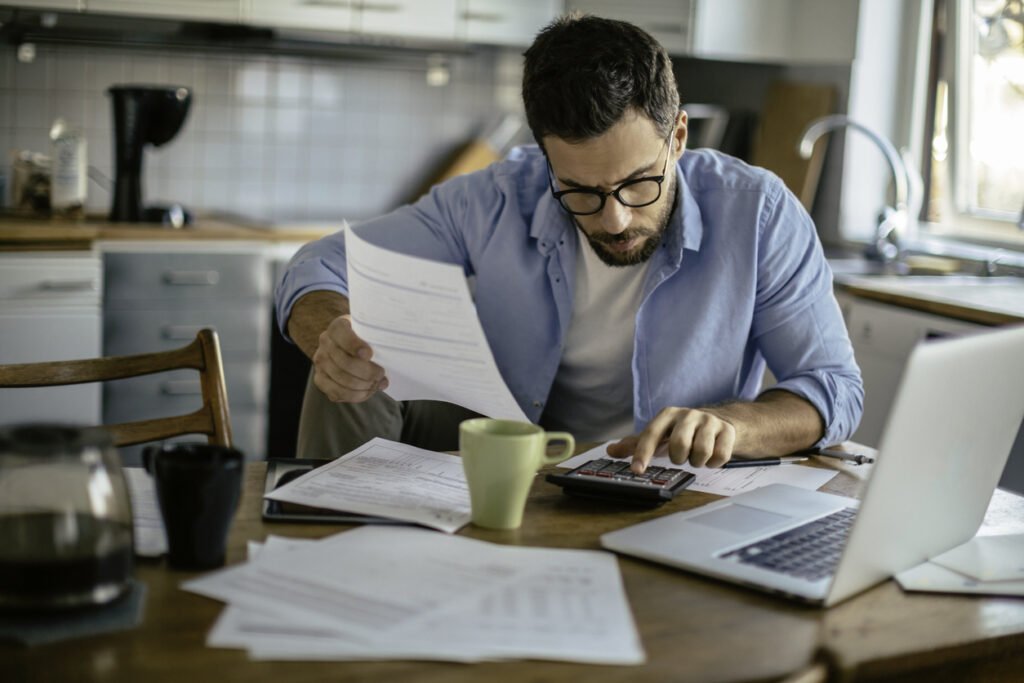 Un homme concentré sur des papiers sur sa table de cuisine, évoquant le télétravail ou la gestion des affaires personnelles.