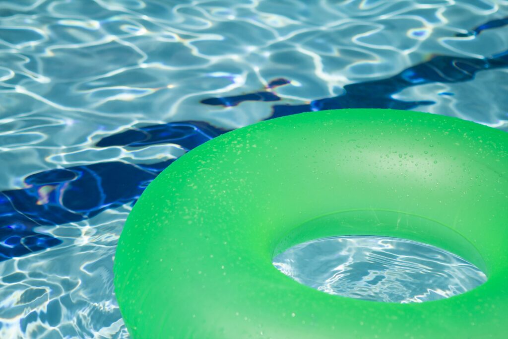 Un flotteur de piscine vert sur l'eau bleue scintillante, évoquant détente et loisirs d'été. Un cadre de porte non fini dans une pièce en rénovation avec une échelle et des outils à proximité, suggérant des travaux de construction en cours.