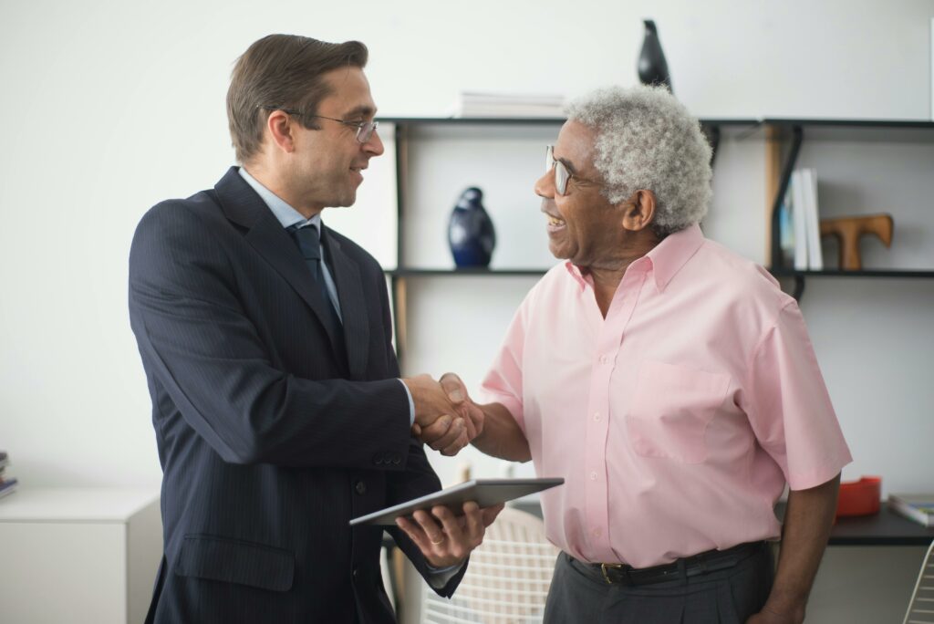 Un professionnel en costume serre la main d'une personne âgée, un échange qui semble chaleureux et pourrait indiquer un accord ou une reconnaissance.