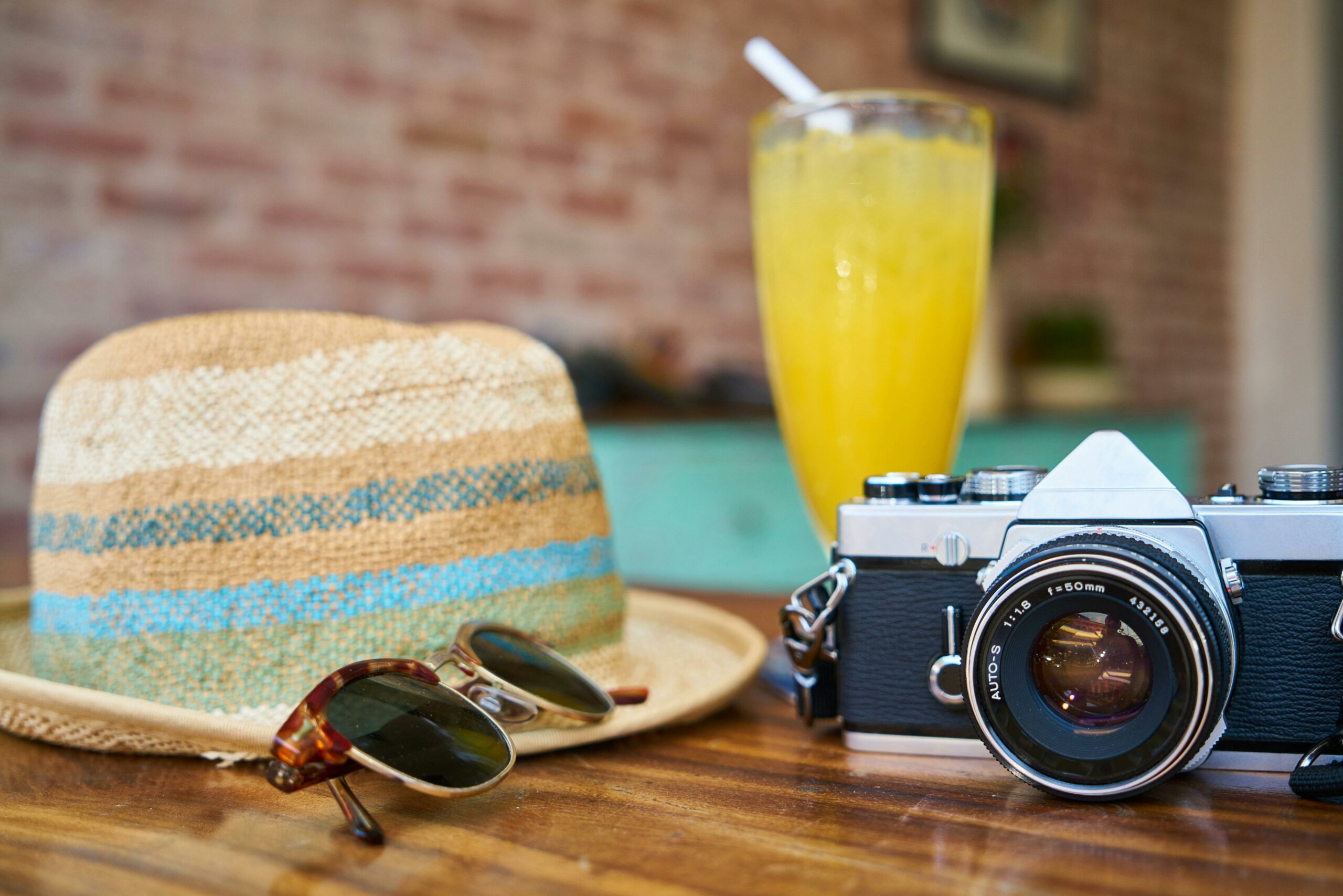 Une table avec un appareil photo vintage, des lunettes de soleil, un chapeau et un verre de boisson fraîche, évoquant une atmosphère de voyage et d'aventure.