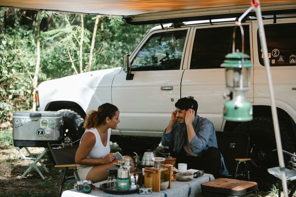 Deux personnes assises à une table de camping en forêt, créant une ambiance détendue et naturelle de vacances en plein air.