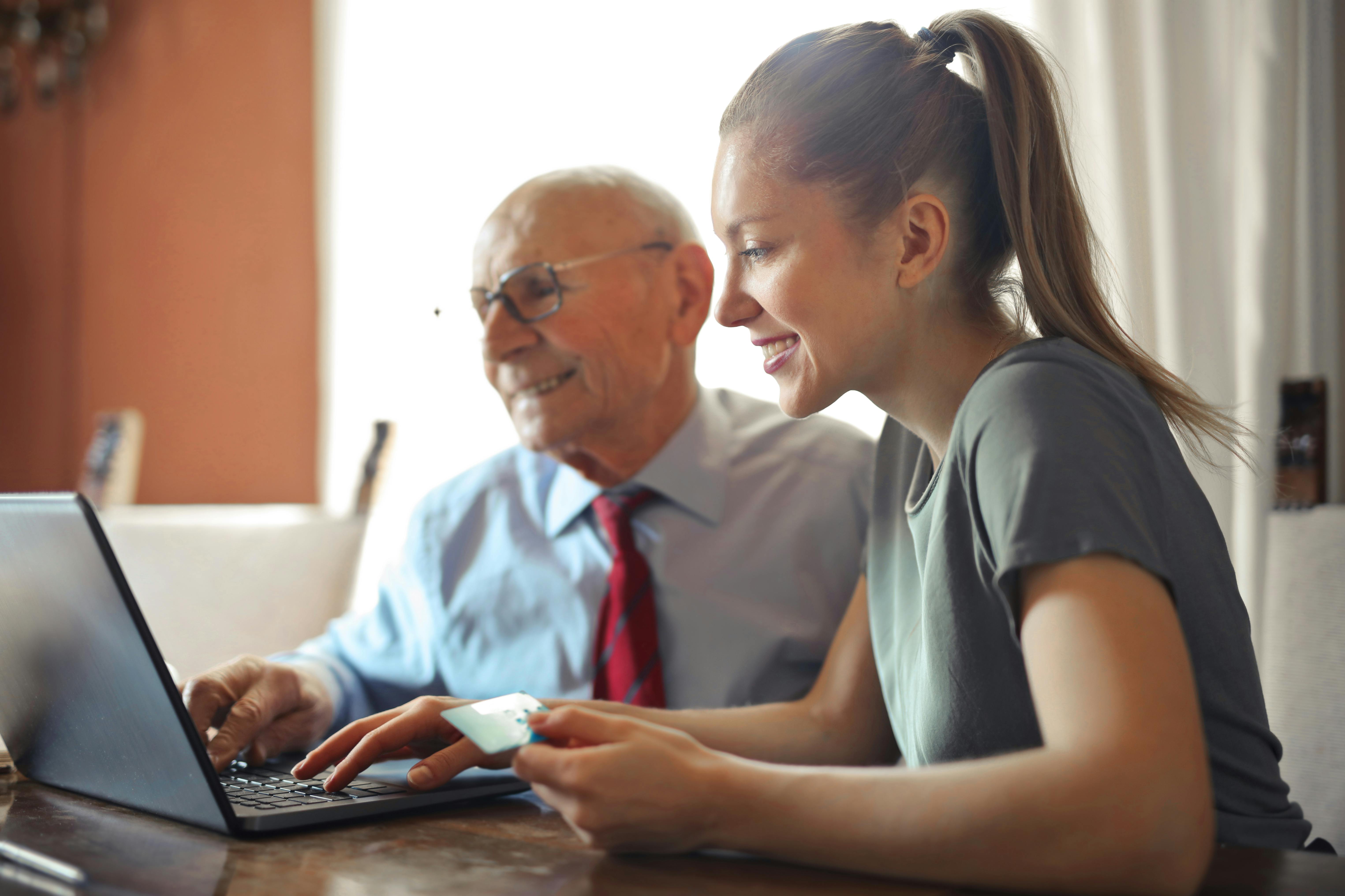 Une jeune femme enseigne l'utilisation d'un ordinateur à un homme âgé, illustrant l'apprentissage intergénérationnel.