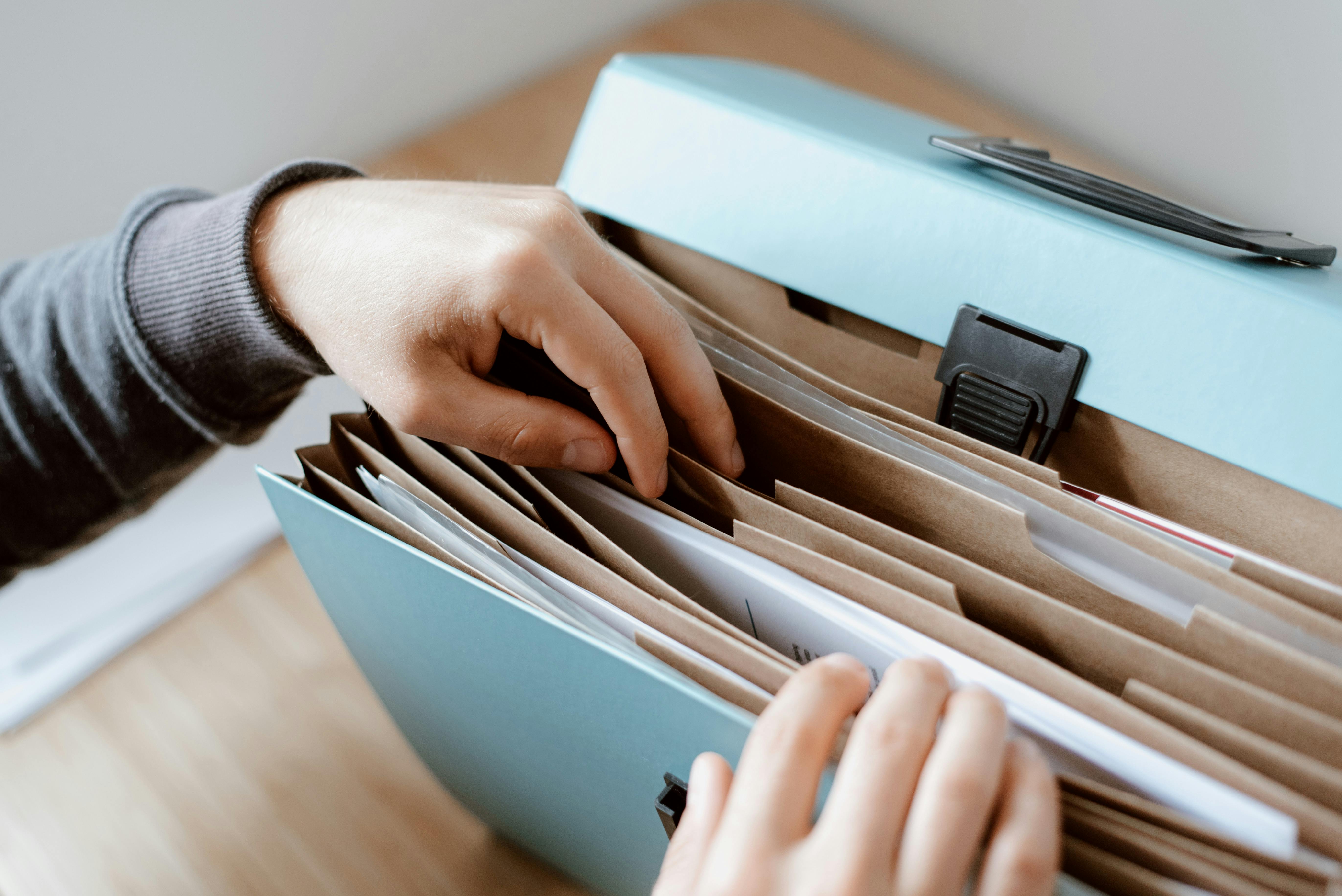 Une personne organise des documents dans une boîte d'archives, dépeignant les tâches administratives quotidiennes dans un bureau.
