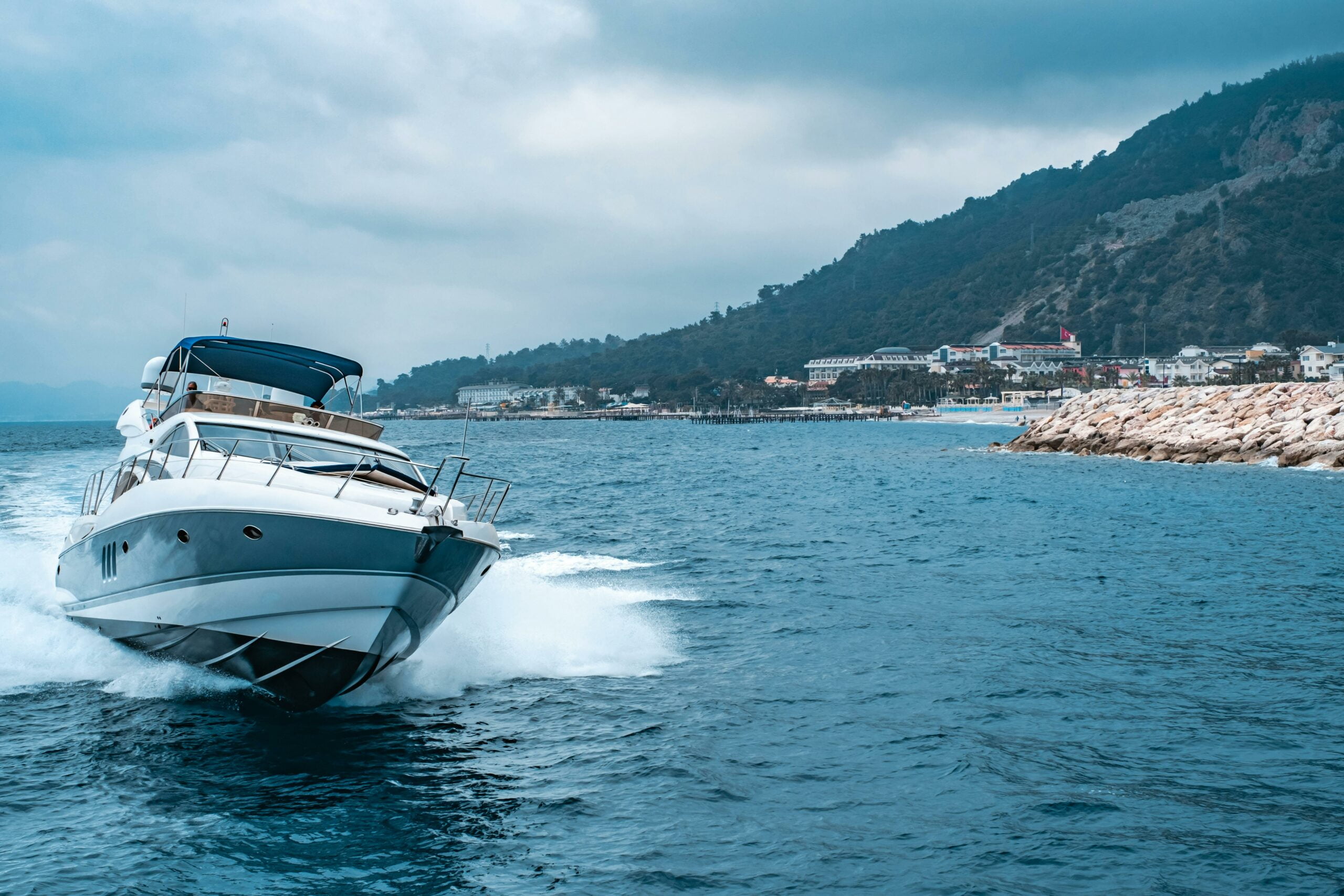 Un yacht naviguant rapidement sur l'eau près d'une côte montagneuse, projetant une sensation de luxe et d'aventure.
