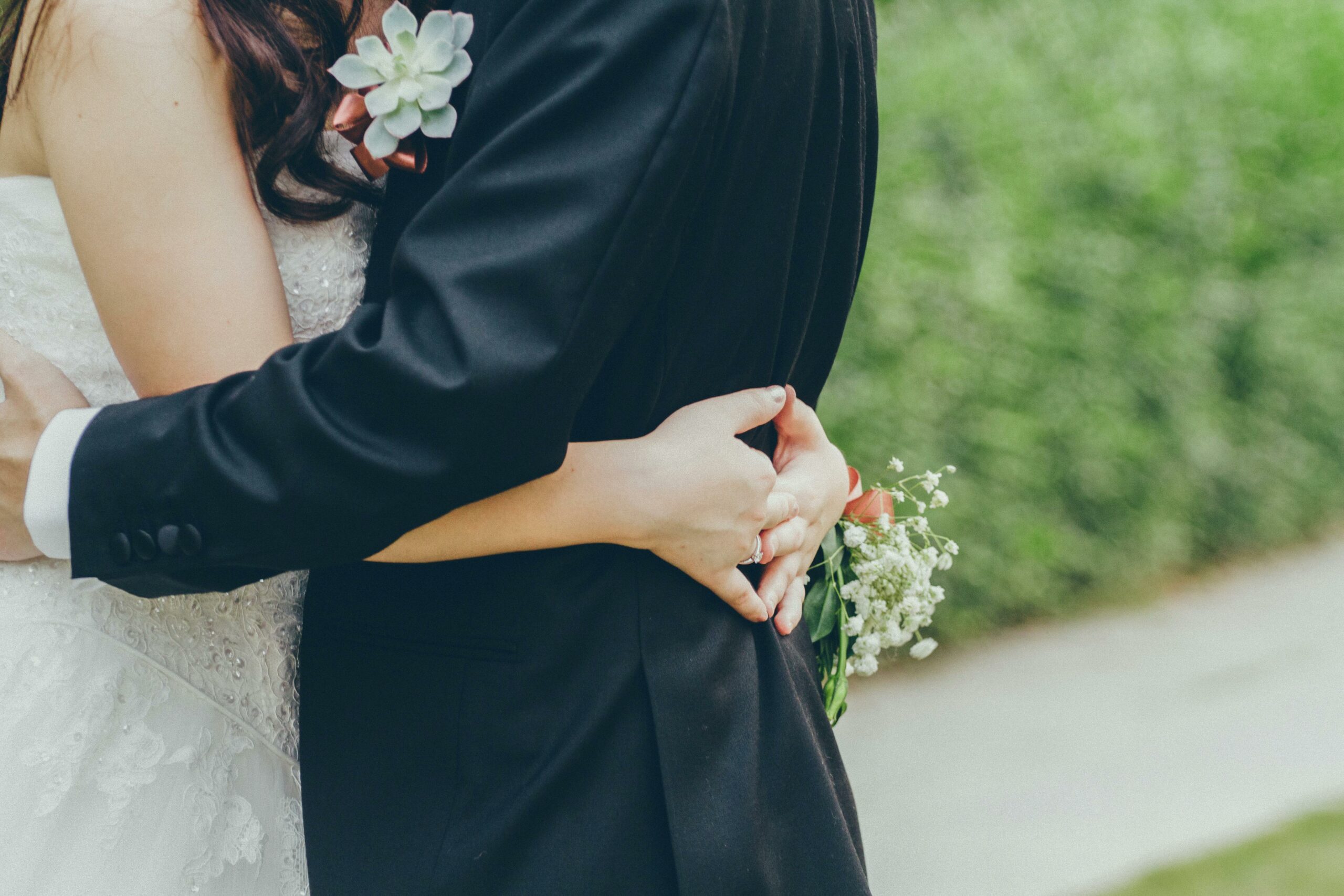 Une étreinte entre marié et mariée, se concentrant sur les mains de la femme tenant un bouquet, capturant un moment intime de célébration.