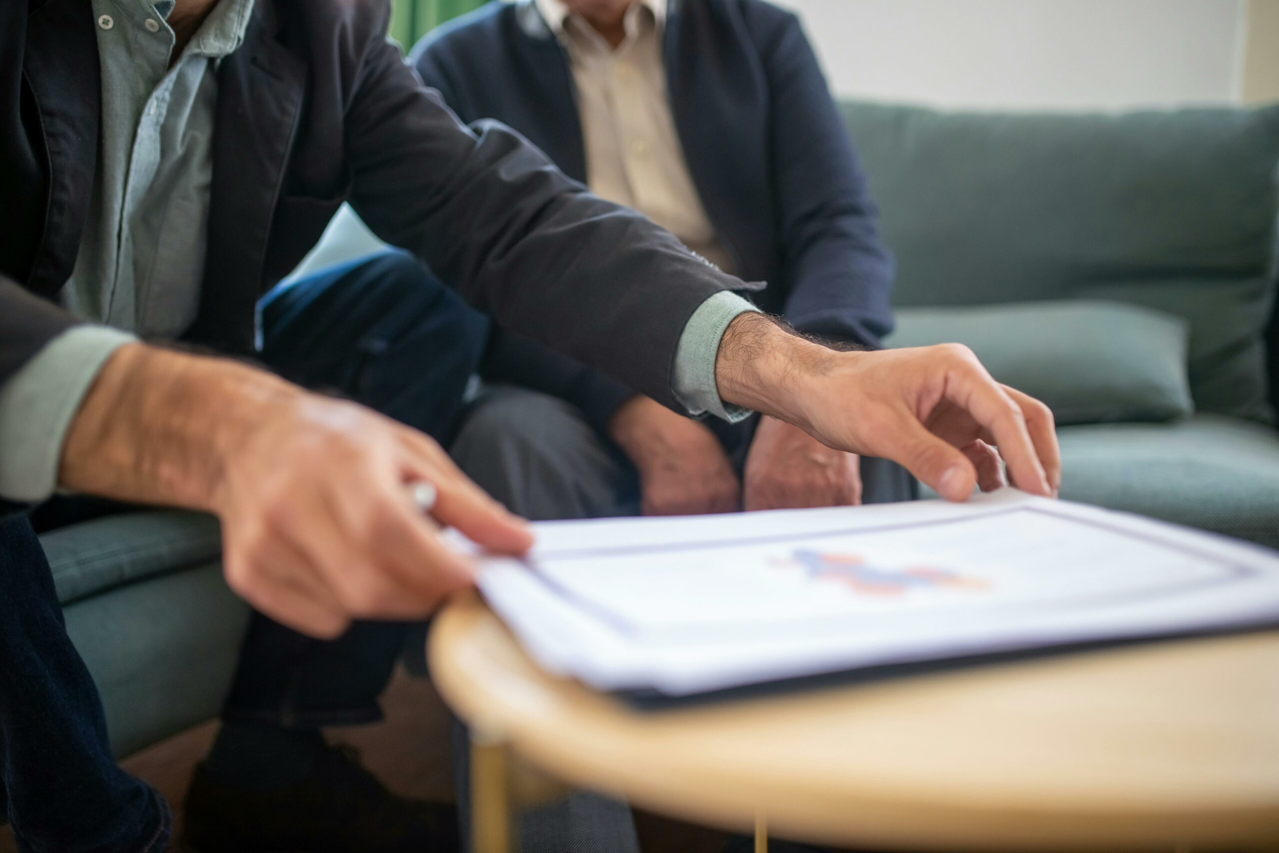 Un homme montre des détails sur un graphique à un autre, dans un salon, représentant une discussion décontractée mais informative sur des performances ou des résultats.