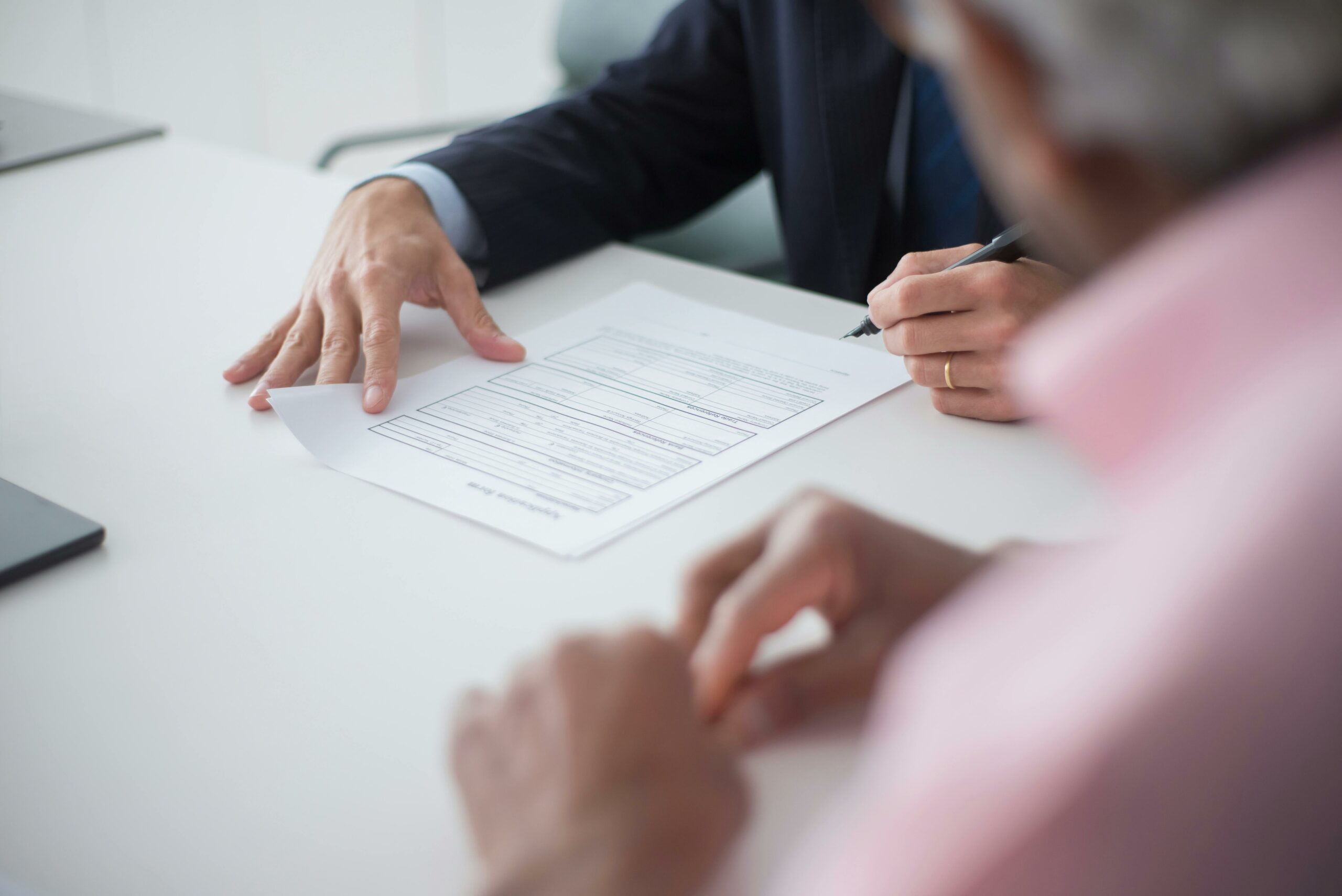 Discussion sérieuse sur des documents, avec un homme âgé pointant du doigt un papier, dans un contexte de réunion ou de consultation.