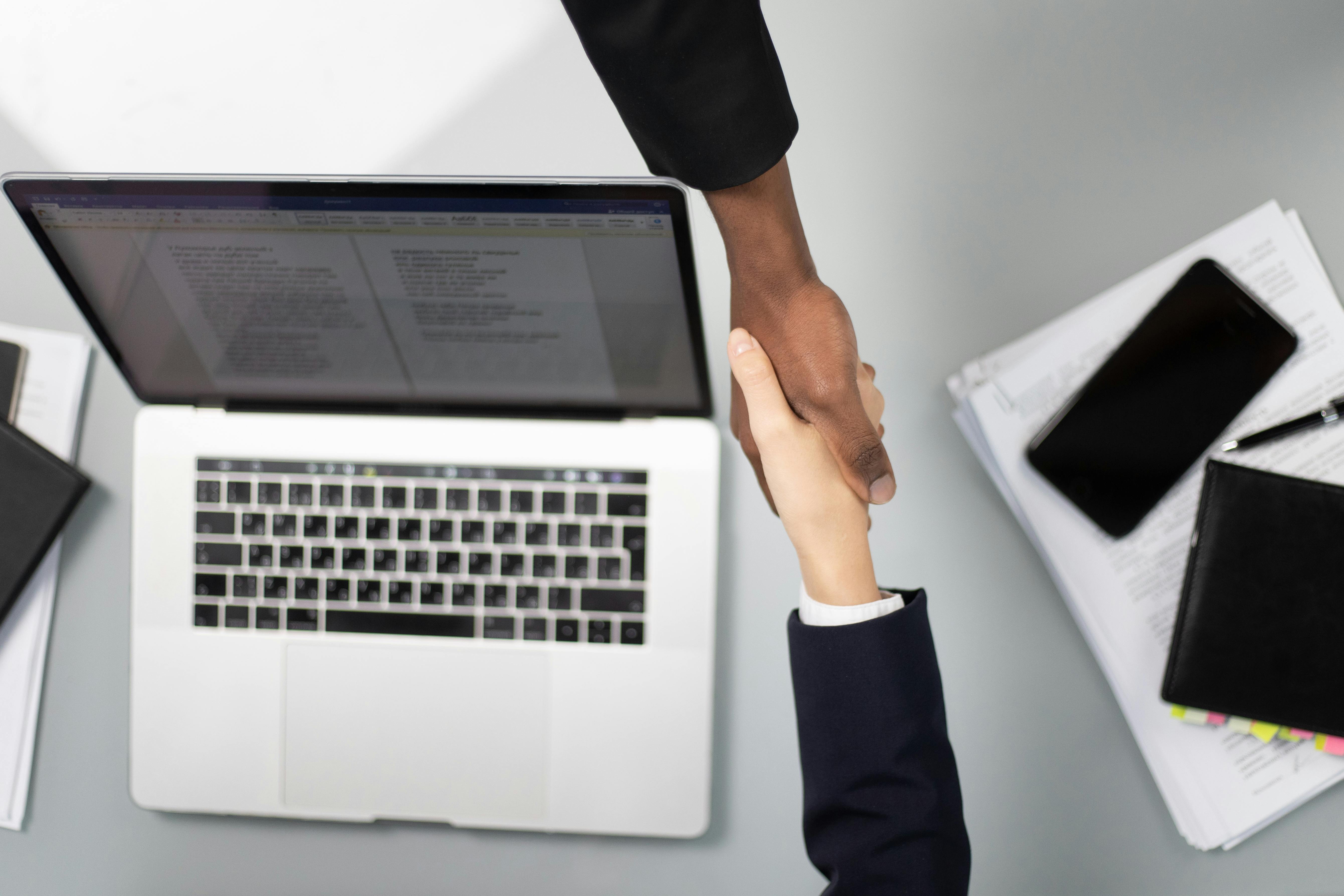 Deux personnes se serrent la main au-dessus d'un ordinateur portable ouvert, représentant un accord ou une collaboration professionnelle.