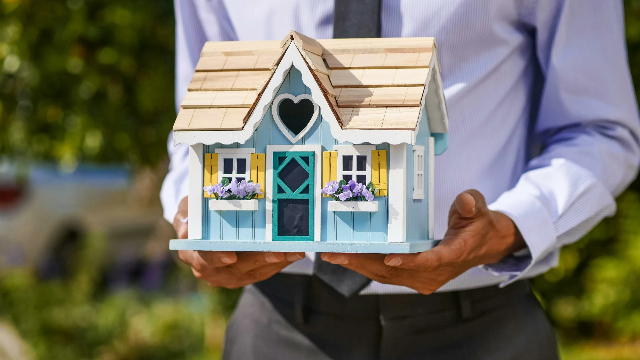 Un homme en costume tenant un modèle de maison colorée, représentant le concept de l'immobilier ou de la propriété personnalisée.