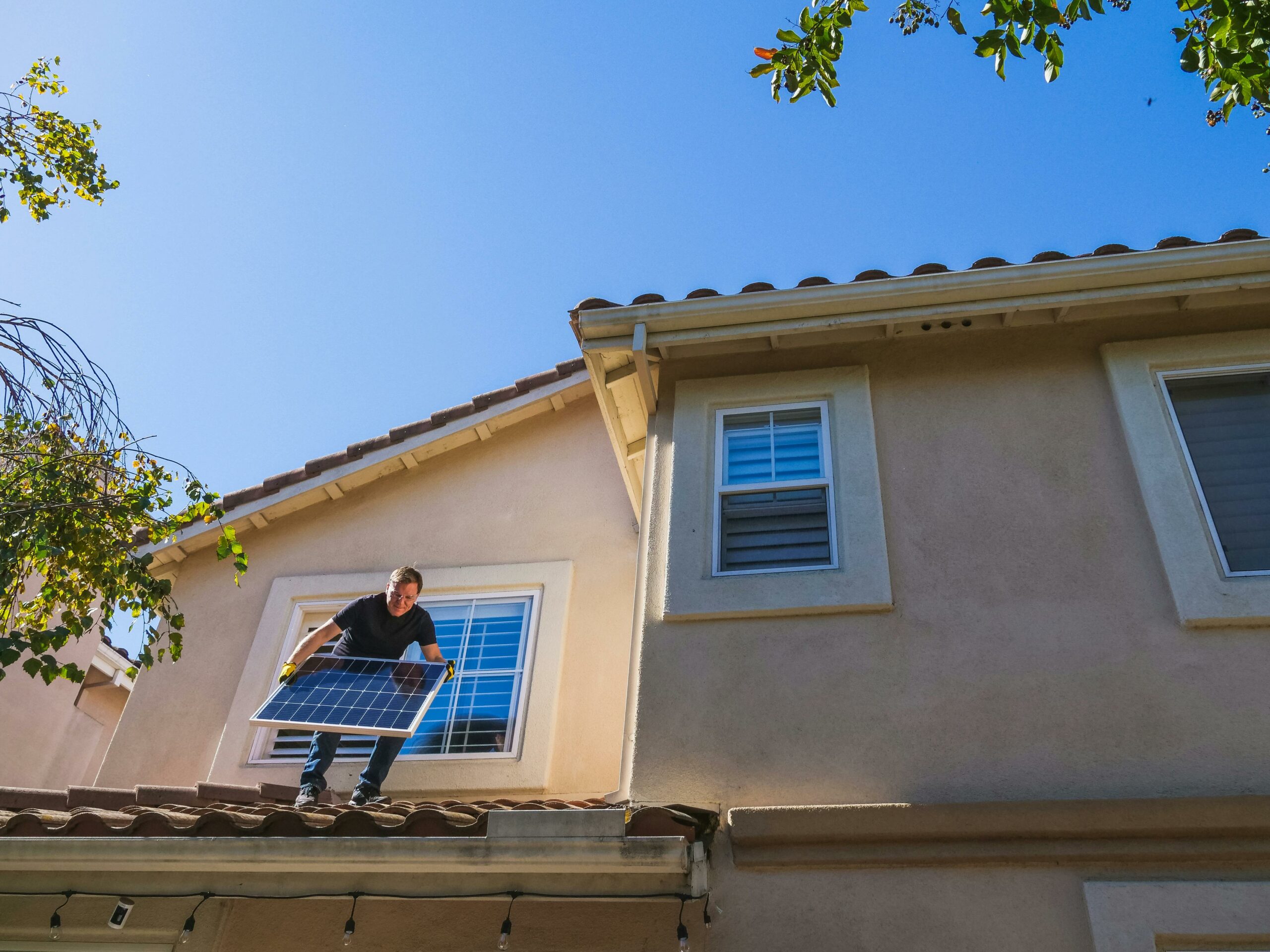 Un homme installe des panneaux solaires sur le toit d'une maison, illustrant l'engagement envers les énergies renouvelables.