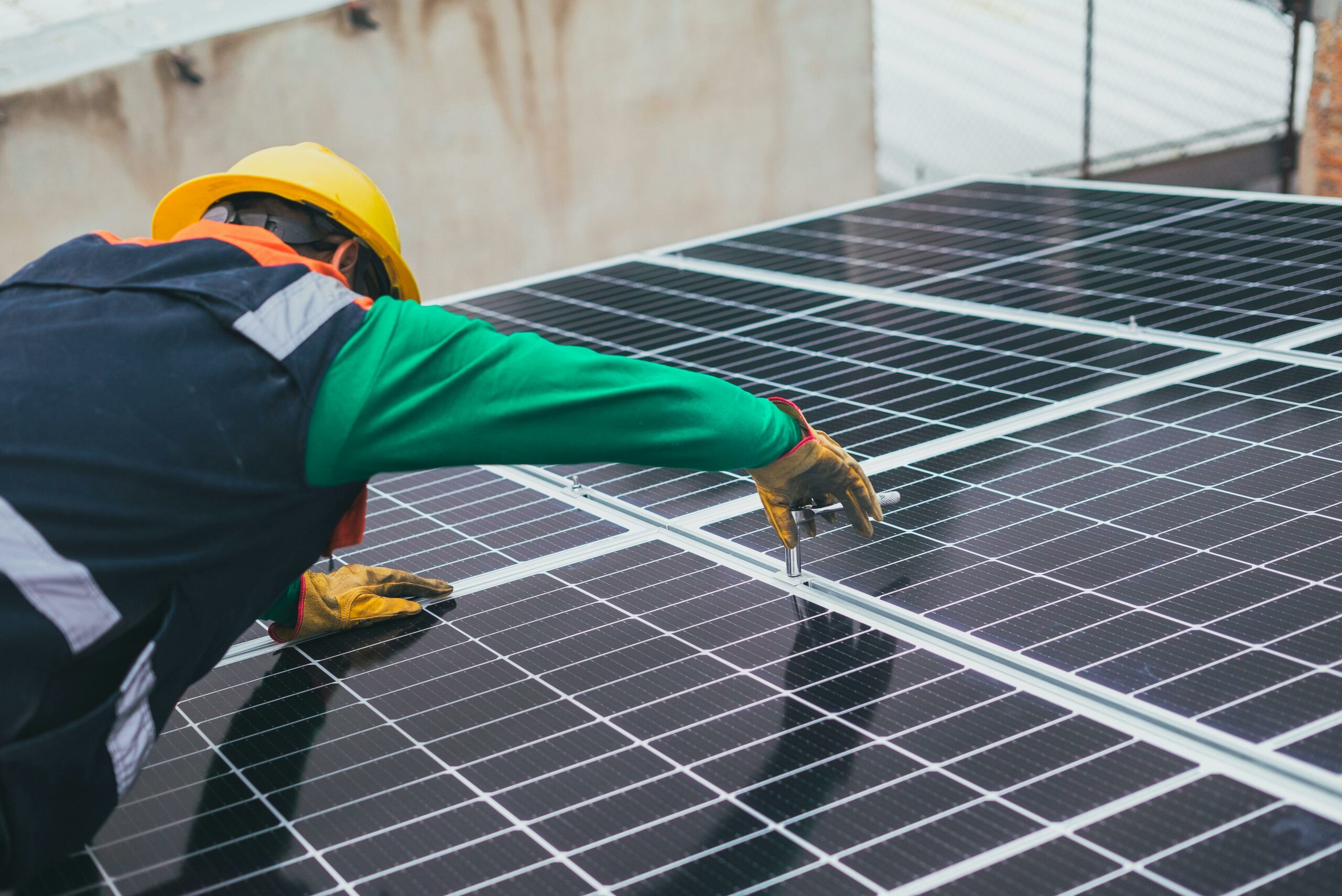 Un ouvrier en tenue de sécurité installe des panneaux solaires sur un toit, mettant en évidence l'importance de l'énergie renouvelable.