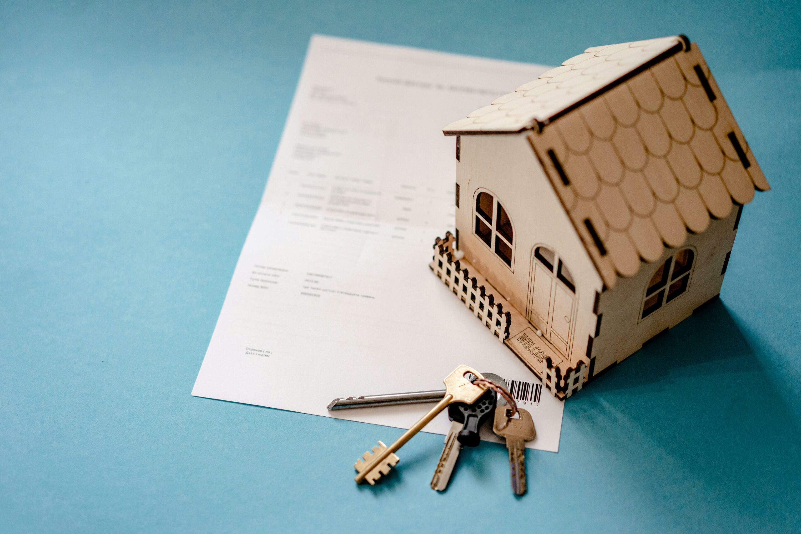 Une petite maison modèle en carton avec un document et des clés à côté, symbolisant l'achat ou la vente d'une propriété.