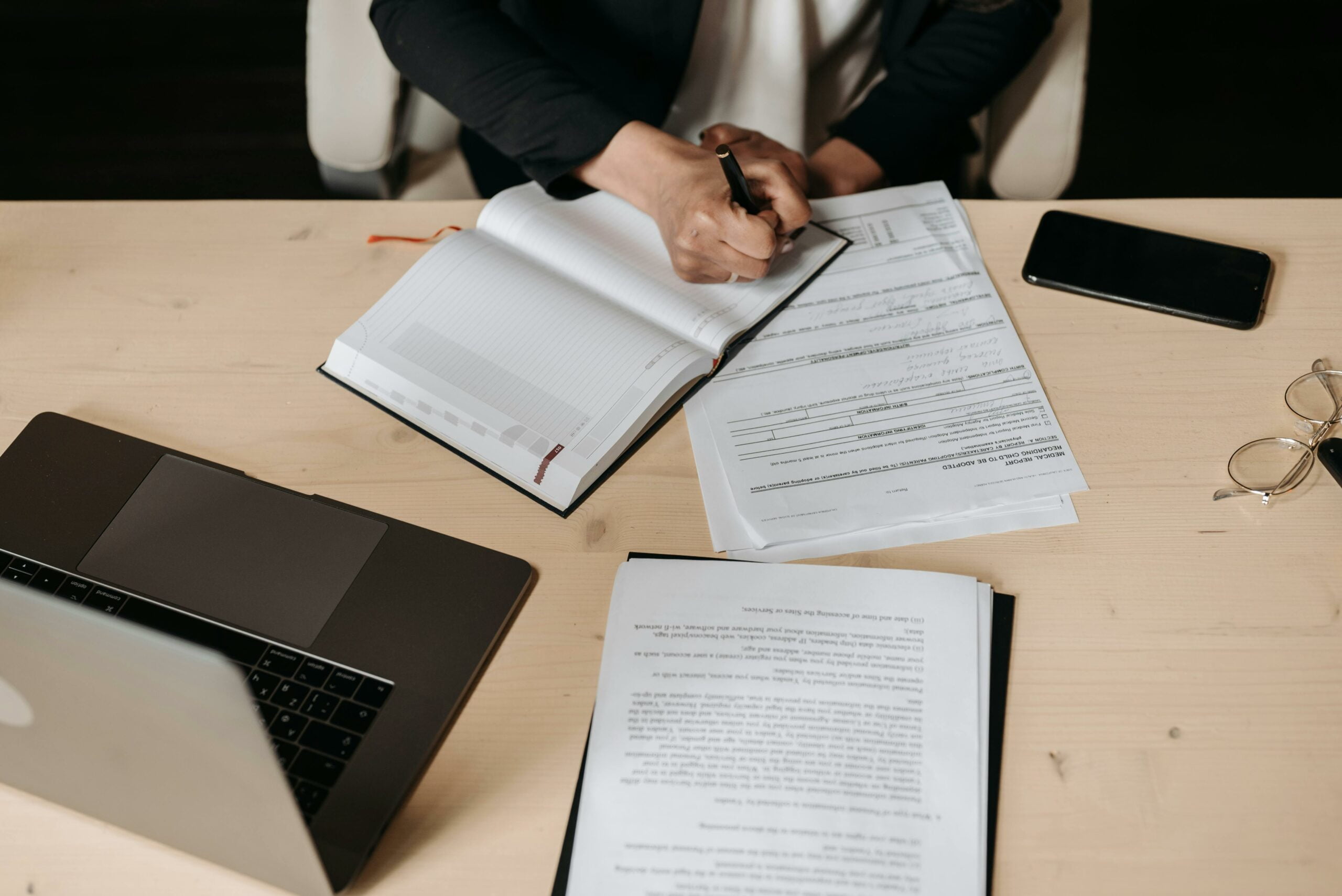 Vue en plongée sur un bureau où une personne tamponne un document, à côté d'un ordinateur portable et d'autres papiers, illustrant une tâche administrative.