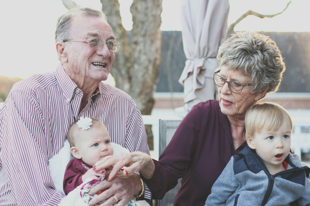 Un couple âgé souriant, tenant chacun un petit enfant, évoquant un moment familial chaleureux et joyeux