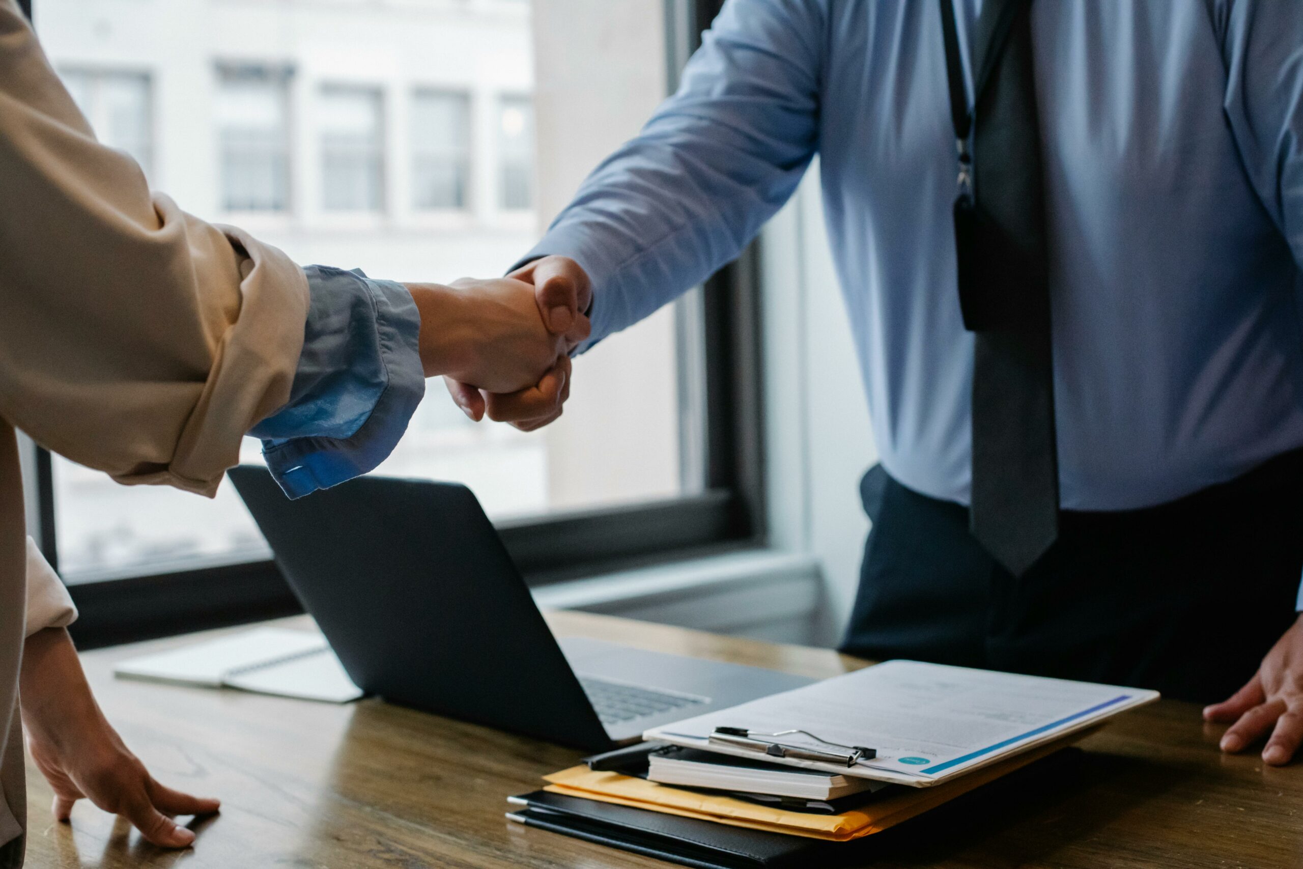 Poignée de main entre deux professionnels au-dessus d'une table de travail, symbole d'un accord ou d'une transaction réussie.