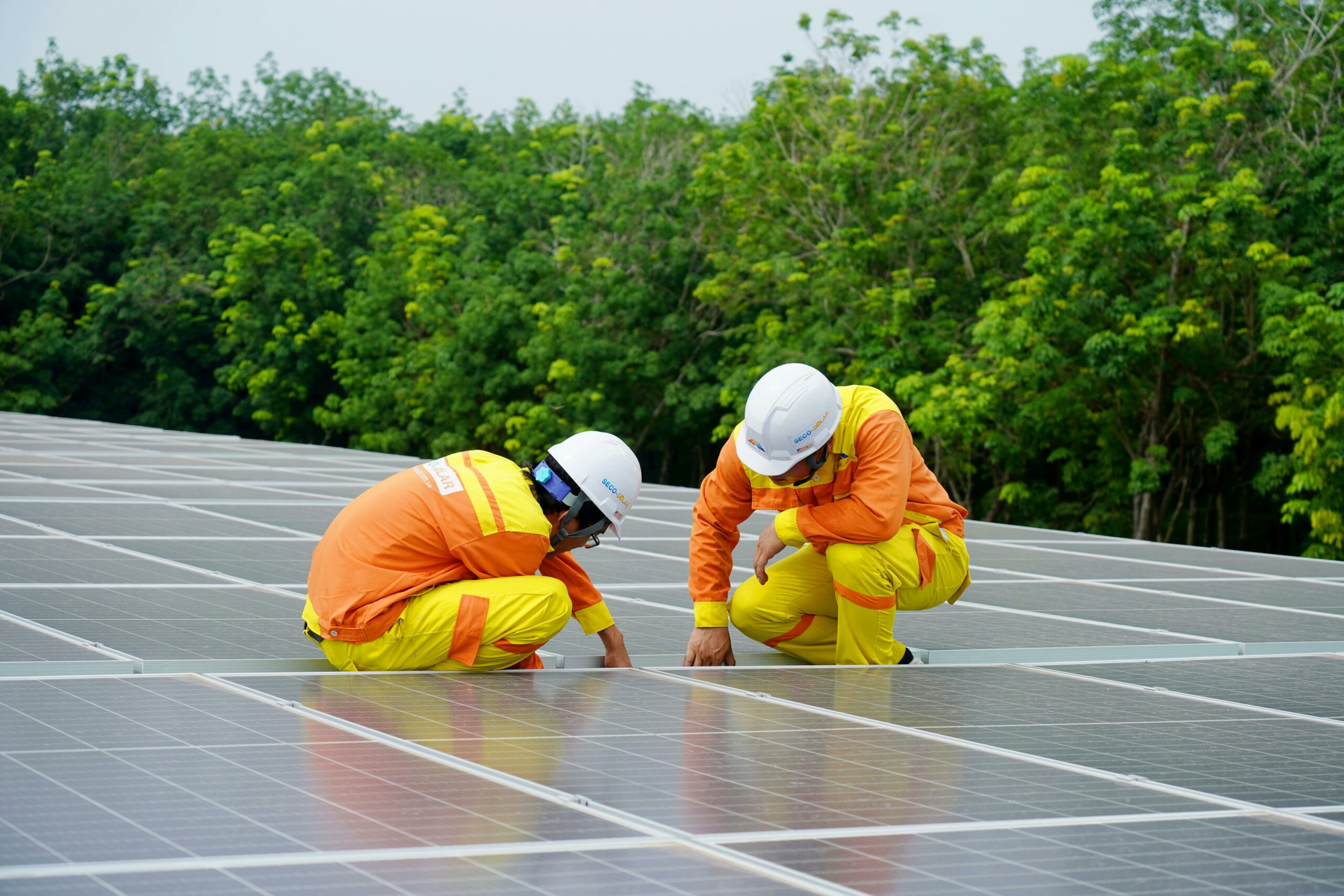 Deux travailleurs en vêtements de sécurité jaunes inspectent des panneaux solaires sur un large toit, illustrant le travail d'équipe dans le secteur de l'énergie renouvelable.