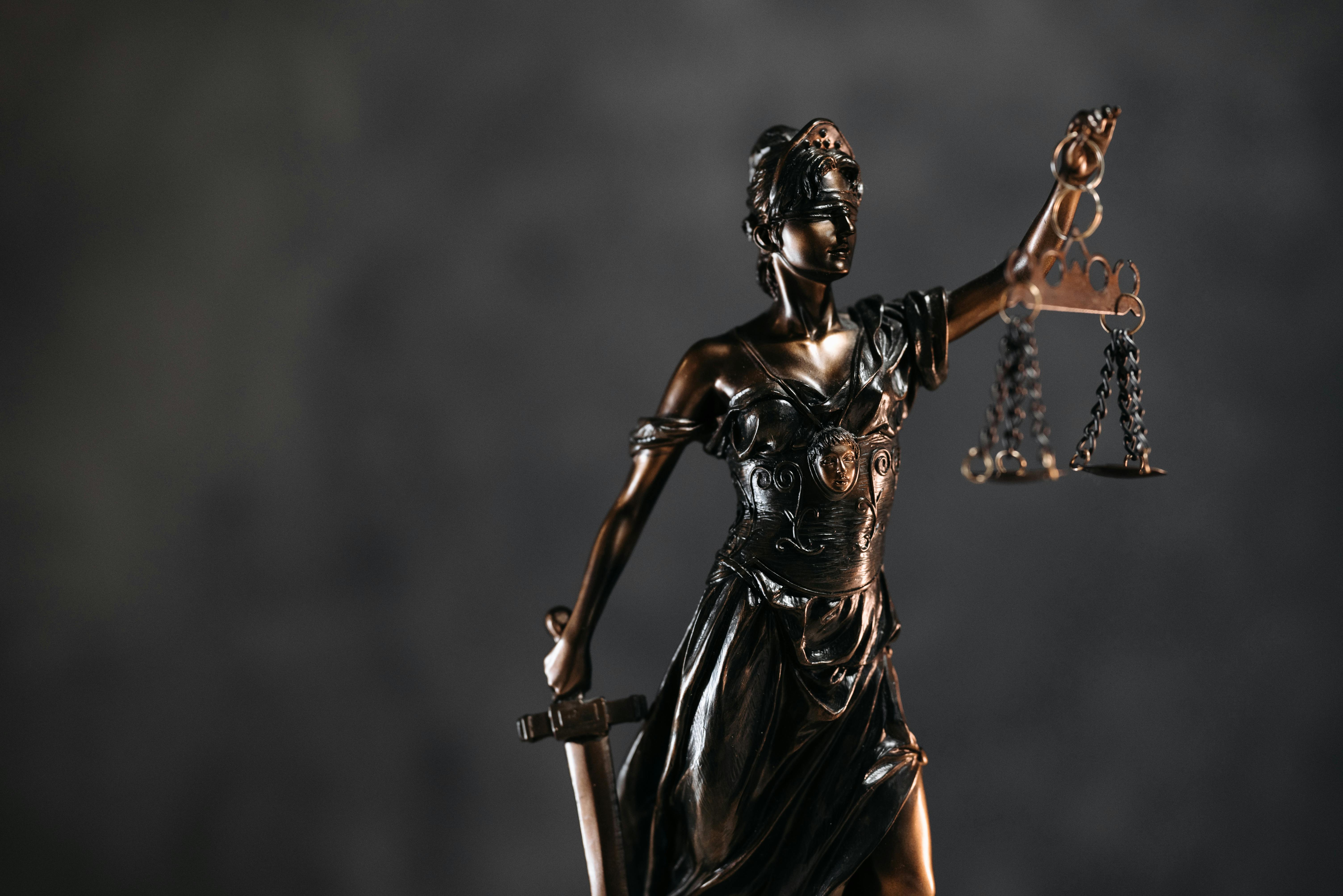 Une statue en bronze de la déesse de la justice, Thémis, tenant une balance dans une main et une épée dans l'autre, avec un bandeau sur les yeux, sur un fond sombre.